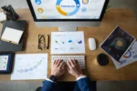 Empreendedor analisando dashboards financeiros no computador, com gráficos e planilhas sobre a mesa — gestão financeira inteligente para empreendedores.