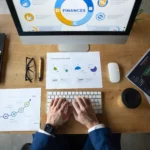 Empreendedor analisando dashboards financeiros no computador, com gráficos e planilhas sobre a mesa — gestão financeira inteligente para empreendedores.