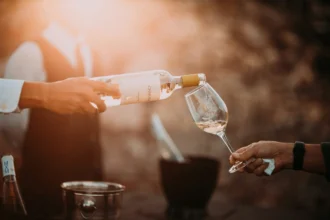 Mão servindo vinho branco em taça ao ar livre, luz dourada ao pôr do sol — inspiração para receitas com vinho branco.