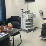 Consultório moderno de otorrinolaringologia com equipamentos médicos e modelos anatômicos sobre a mesa.