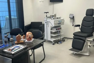 Consultório moderno de otorrinolaringologia com equipamentos médicos e modelos anatômicos sobre a mesa.