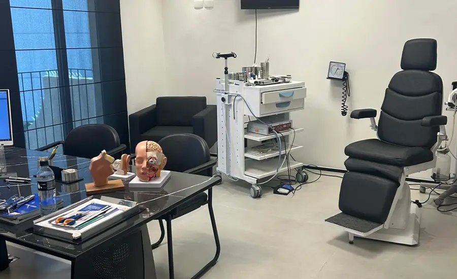 Consultório moderno de otorrinolaringologia com equipamentos médicos e modelos anatômicos sobre a mesa.